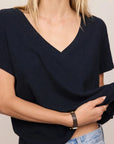 Person wearing a black V-neck top and blue jeans against a neutral background