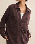 Person wearing a dark brown button-up shirt with pockets on a beige background