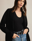 Woman wearing a black cardigan over a black top and blue jeans on a beige background