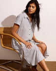 Woman sitting on a chair wearing a light gray dress with a white background