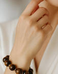 Close-up of a hand wearing a brown beaded bracelet on a white background