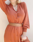 Person wearing a long rust-colored dress with a belt against a light background