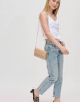 Woman wearing a white top and light blue jeans with a beige handbag on a plain background