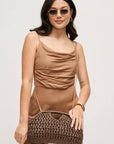Woman wearing a brown dress holding a matching handbag against a light gray background