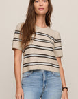 Woman wearing a beige sweater with black stripes and blue jeans on a plain background