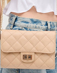 Beige quilted handbag with gold chain strap worn by a person in jeans and a white top.