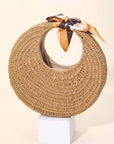 Woven hat with a ribbon on a white stand against a beige background