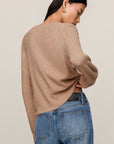Person wearing a beige sweater and blue jeans against a plain background