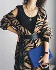Person wearing a black and brown patterned cardigan holding a blue clutch against a neutral background