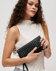 Woman holding a black woven clutch against a plain background