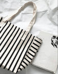 Black and white striped tote bag on a white surface with a notebook.