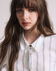 Woman wearing a white shirt with blue stripes against a plain background