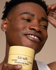 Man holding a jar of 'kit-sch' Treatment Mask against a neutral background