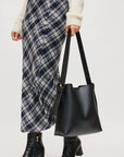 Person holding a black handbag wearing a plaid skirt and black boots on a white background