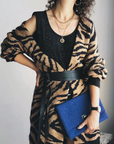 Person wearing a tiger-striped cardigan holding a blue clutch against a neutral background