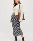 Woman wearing a plaid skirt, white sweater, and black boots on a white background