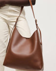 Brown leather handbag held by a person wearing beige pants on a light background