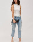 Woman wearing a white sleeveless top and blue jeans on a plain background