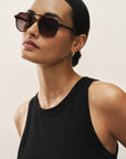 Woman wearing sunglasses and a black tank top against a neutral background