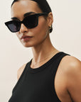 Woman wearing black sunglasses and a black top against a beige background