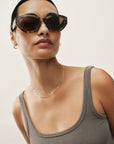 Woman wearing sunglasses and a tank top against a plain background