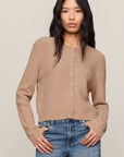 Woman wearing a beige cardigan and blue jeans against a plain background