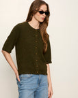Woman wearing a dark green sweater and blue jeans against a plain background