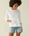 A female model wearing a white slub knit hoodie with a drawcord at the hood and a kangaroo pocket, paired with blue denim shorts.