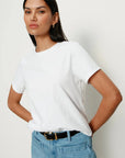Woman wearing a white t-shirt and blue jeans against a plain background