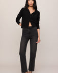 Woman wearing a black button-up shirt and dark jeans against a plain background