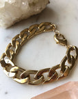 A gold-filled chunky chain bracelet with a lobster clasp, displayed on a white surface with a crystal partially visible to the left.