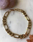 A gold-filled chain bracelet laid out on a marble surface, reflecting light due to its metallic finish.