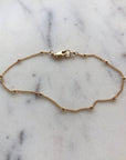 A delicate gold satellite chain bracelet with a total circumference of 7 inches, made of 14k gold filled material, displayed on a marble surface.