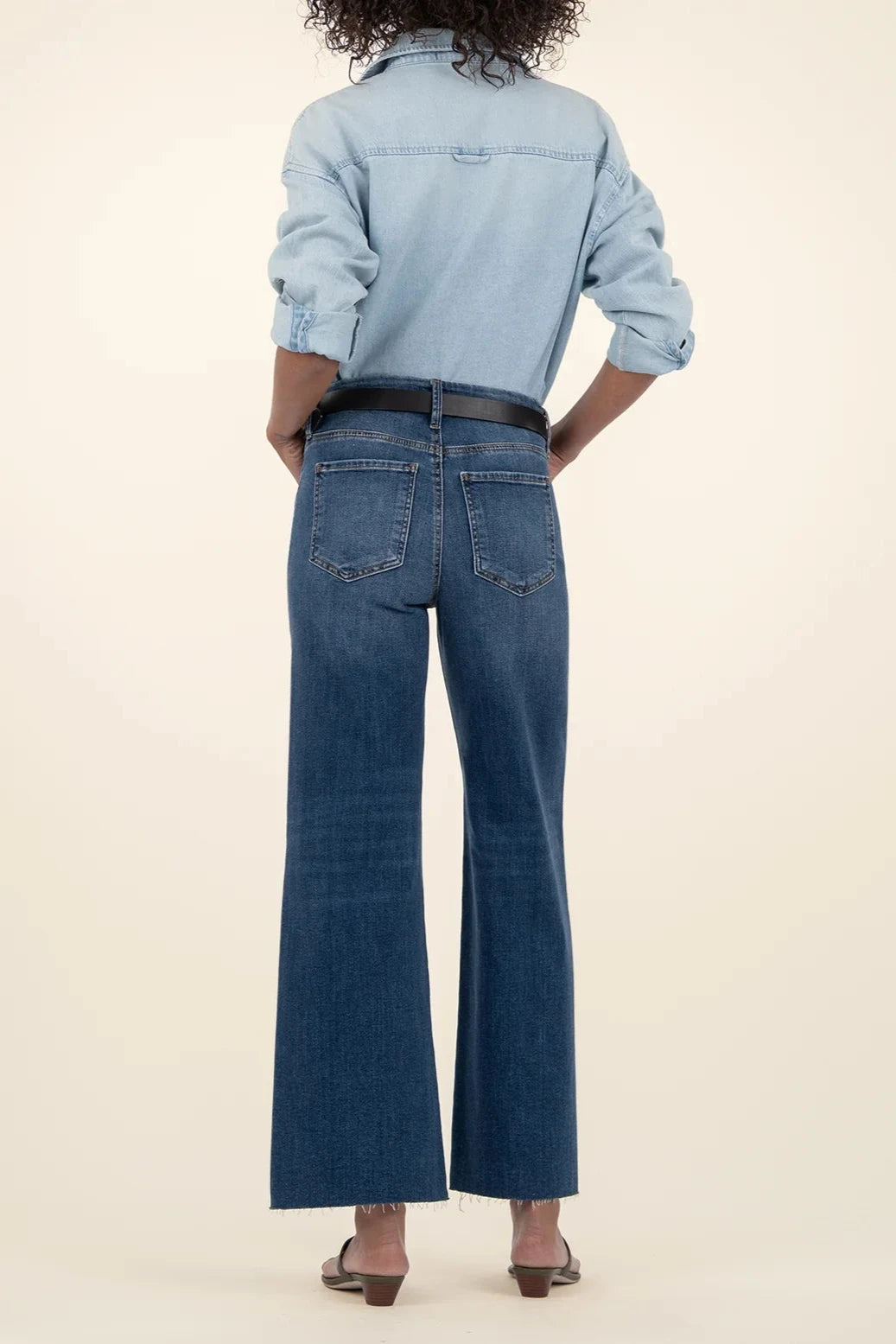 Person wearing a light blue denim shirt and dark blue jeans on a beige background