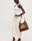 Woman holding a brown leather handbag against a white background