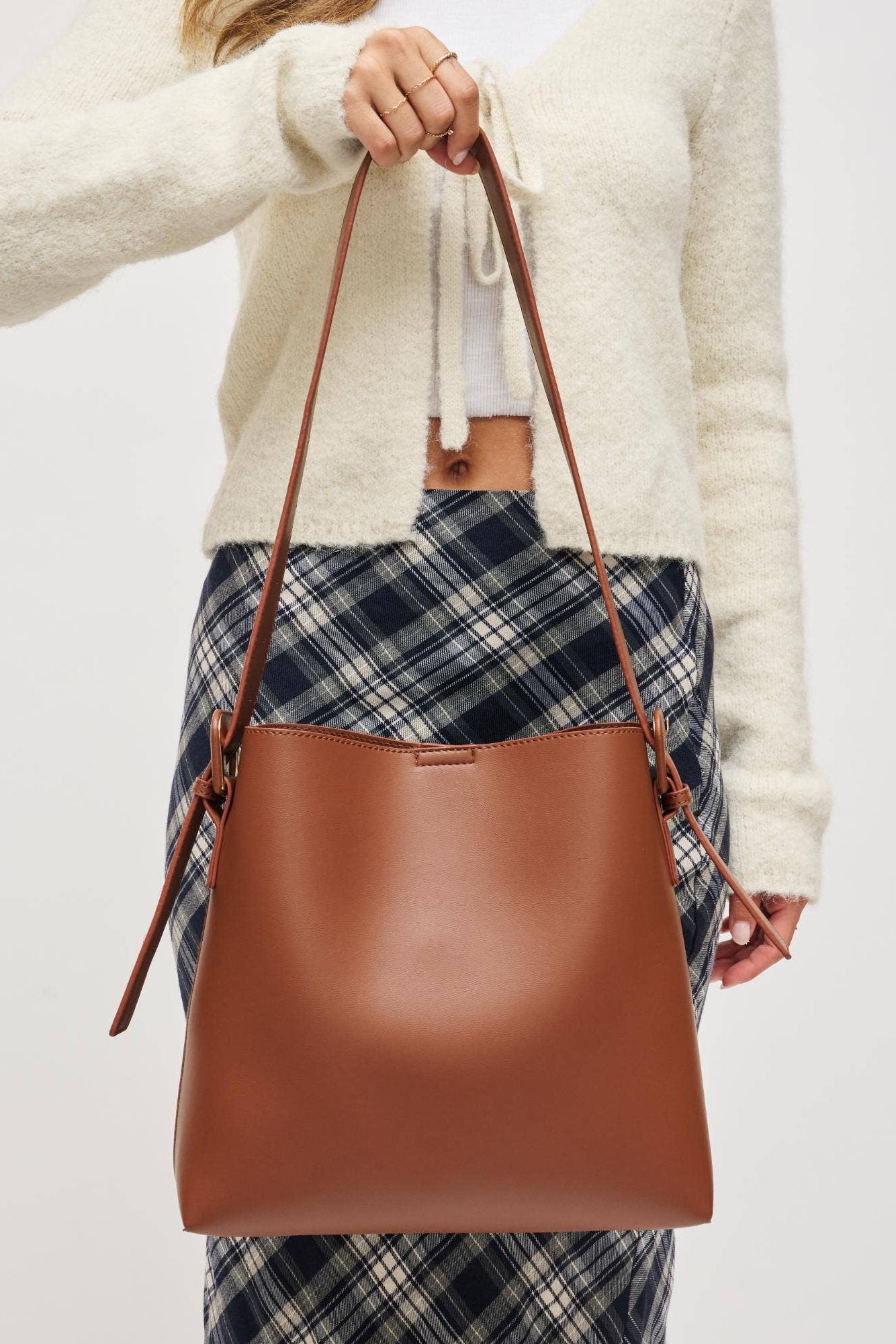 Person holding a brown leather handbag with a plain background