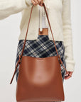 Person holding a brown leather handbag with a plain background