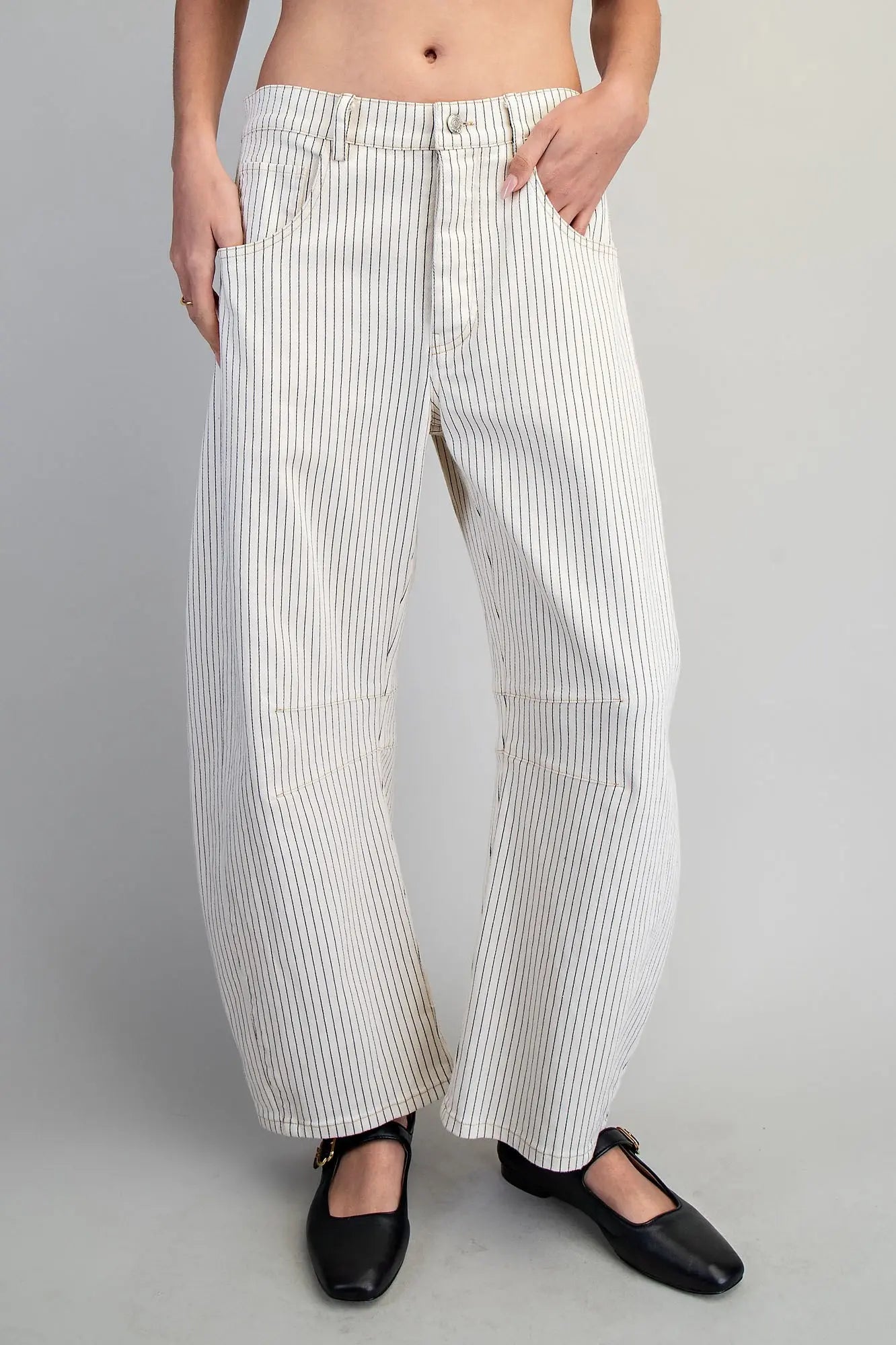A person wearing off-white wide-leg pinstriped pants with black Mary Jane shoes, shown from the waist down against a light gray studio background.