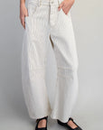 A person wearing off-white wide-leg pinstriped pants with black Mary Jane shoes, shown from the waist down against a light gray studio background.