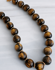 A beaded necklace made of polished tiger's eye beads with gold spacer rings and a gold clasp, displayed on a light gray marble surface.