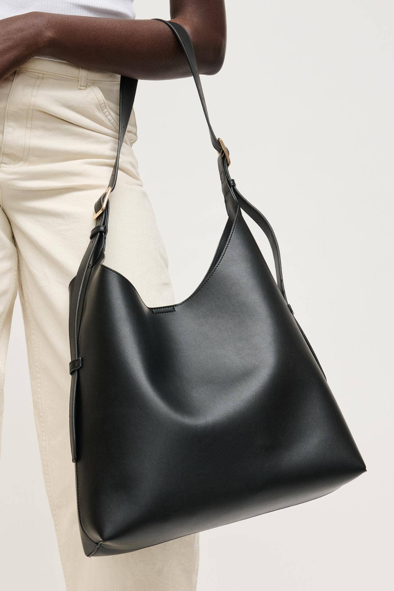 Black leather handbag held by a person wearing beige pants on a light background