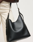 Black leather handbag held by a person wearing beige pants on a light background