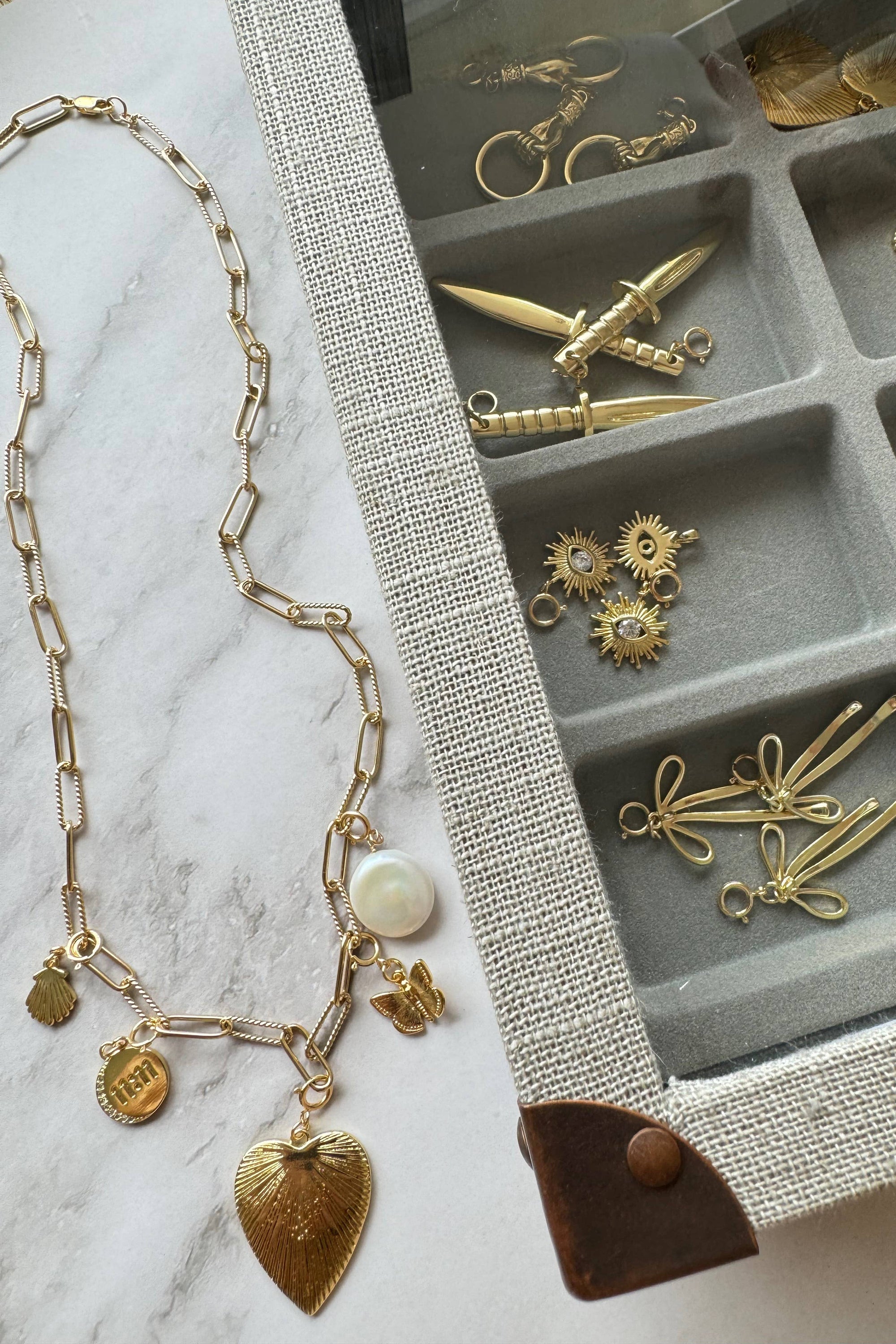 Gold necklace with charms on a marble surface next to an open jewelry box with more gold jewelry pieces.