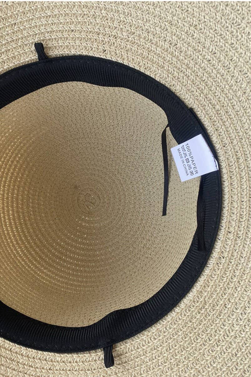 Beige straw hat with black band and tag on a beige background