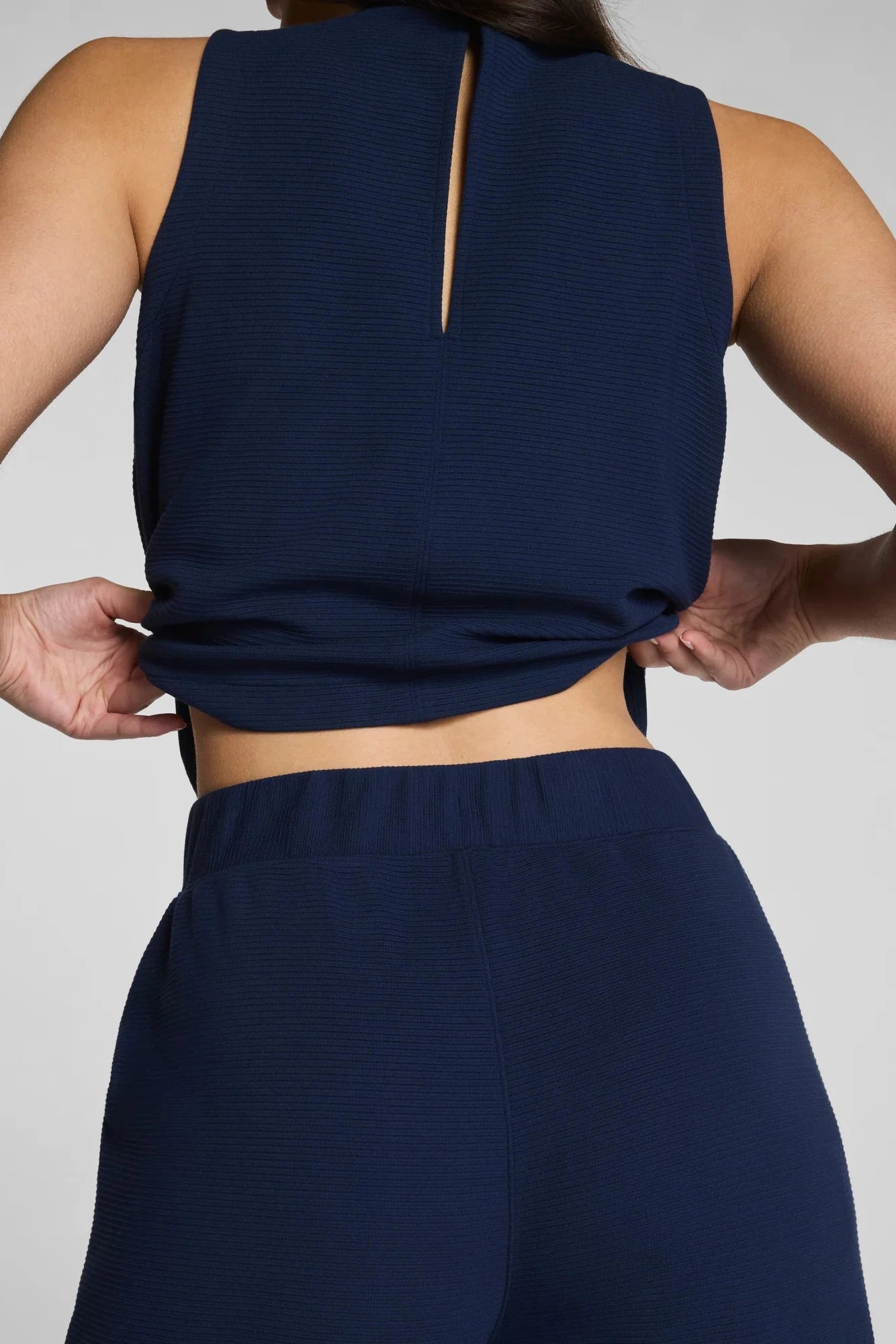 Person wearing a navy blue sleeveless top and pants on a light gray background