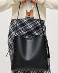 Person holding a black leather bag with plaid skirt and white sweater