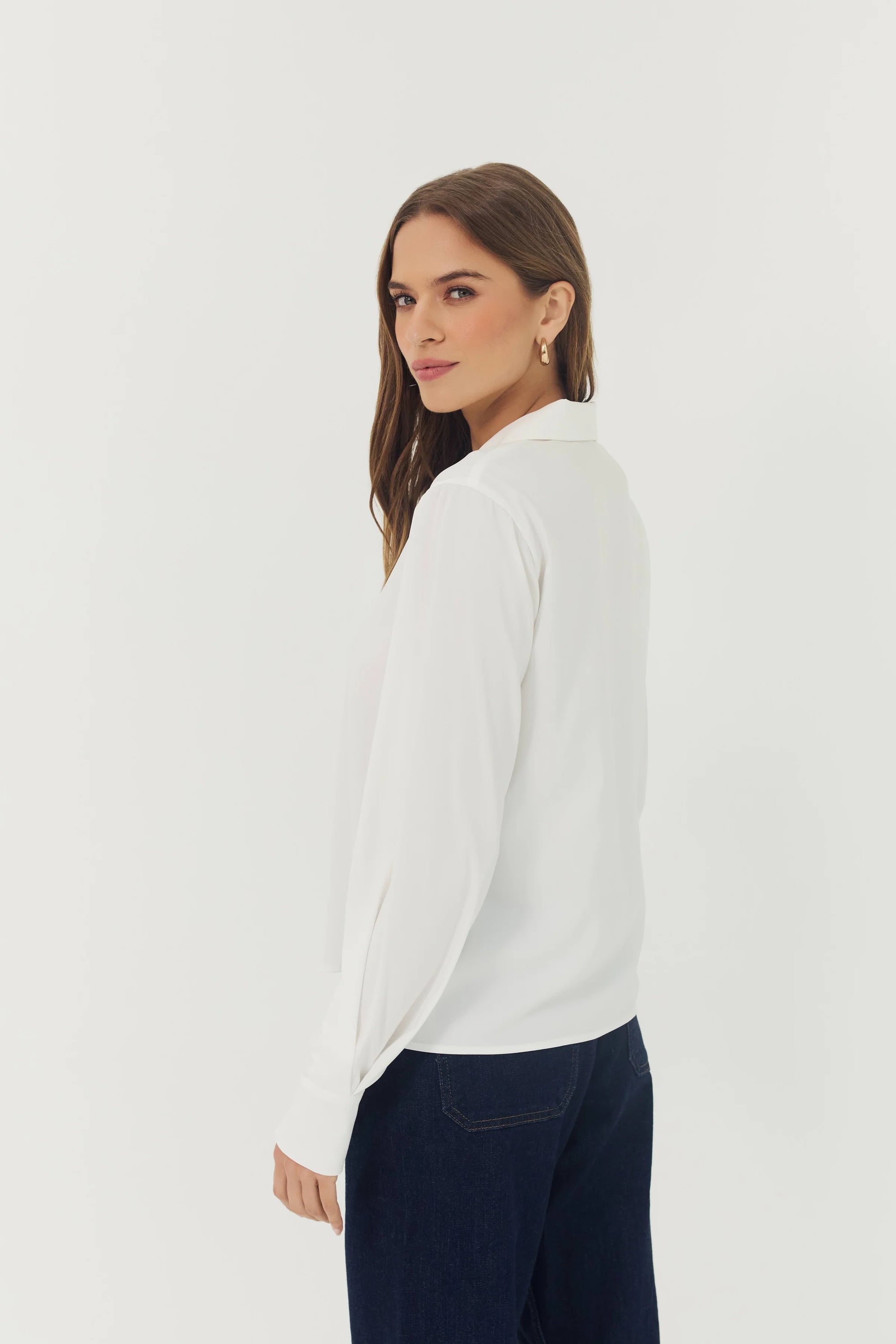 Woman wearing a white blouse and dark pants on a plain background