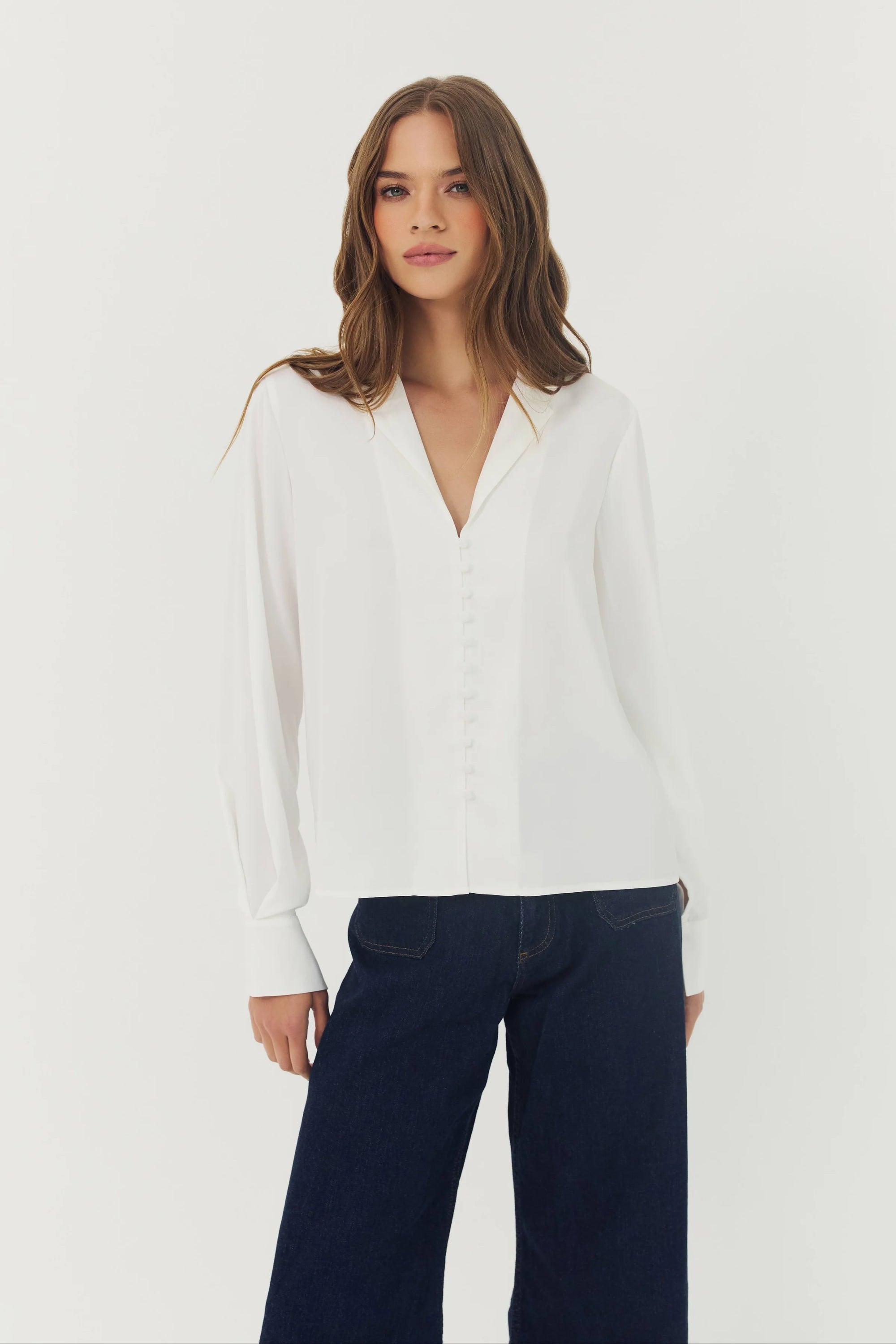 Woman wearing a white blouse and navy pants on a plain background