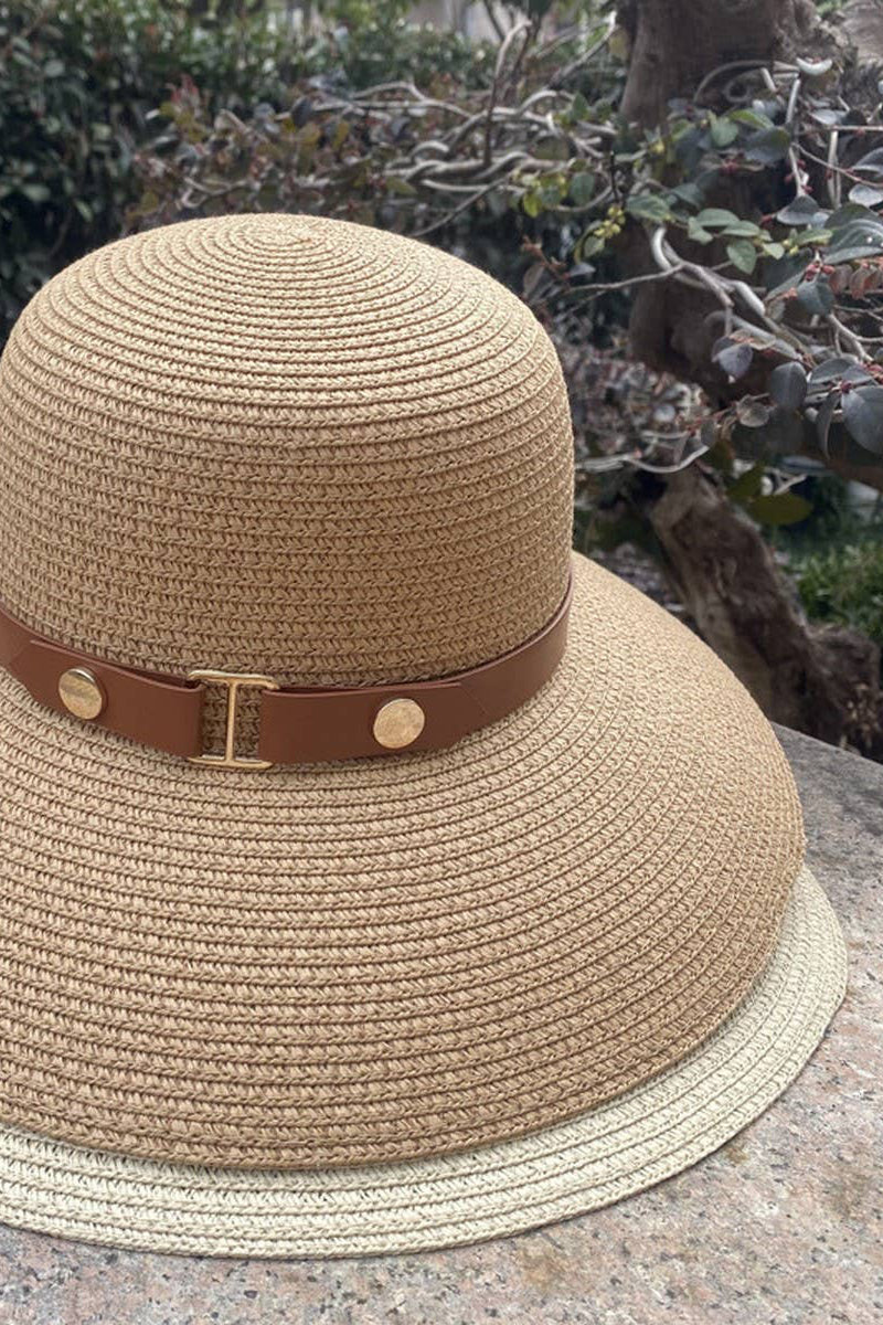 Beige straw hat with a brown band on a stone surface with greenery in the background