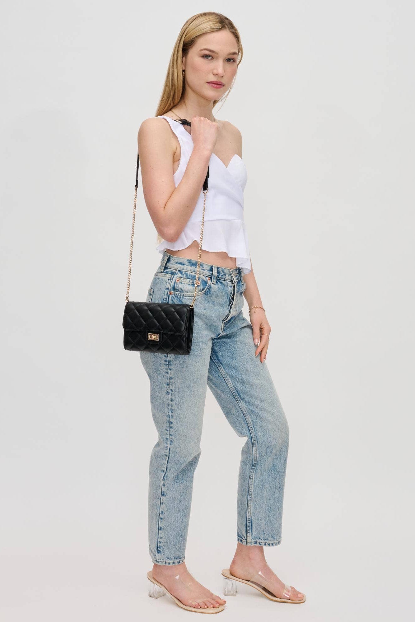 Woman wearing a white top and blue jeans with a black handbag on a light gray background
